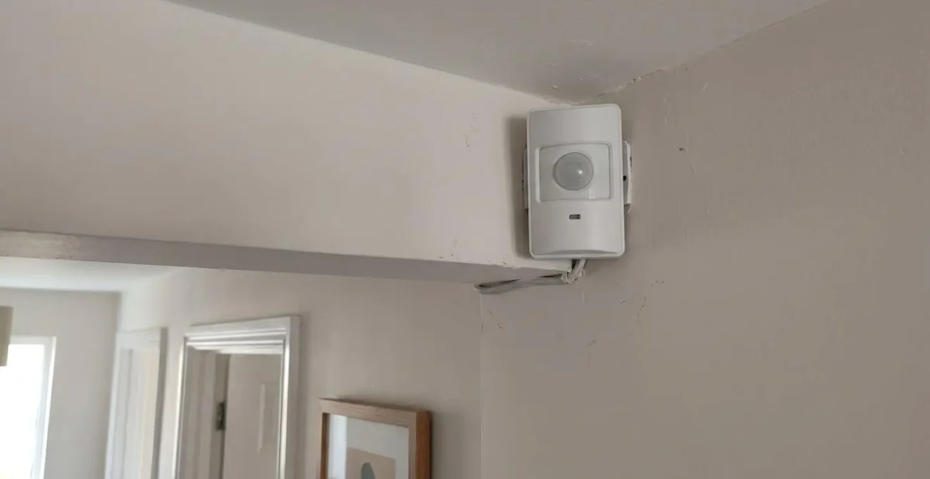 Détecteur de mouvement infrarouge blanc installé dans l'angle supérieur d'une pièce résidentielle avec voyant LED discret