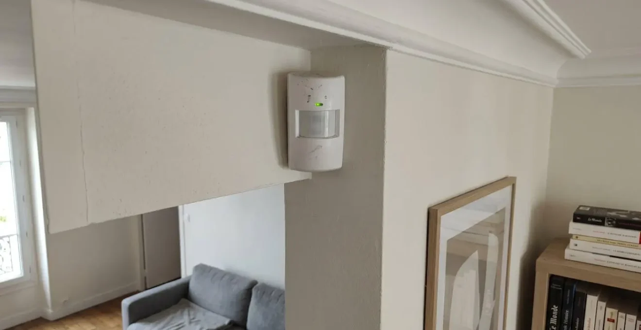 Détecteur de mouvement infrarouge blanc installé dans l'angle supérieur d'une pièce résidentielle avec voyant LED discret
