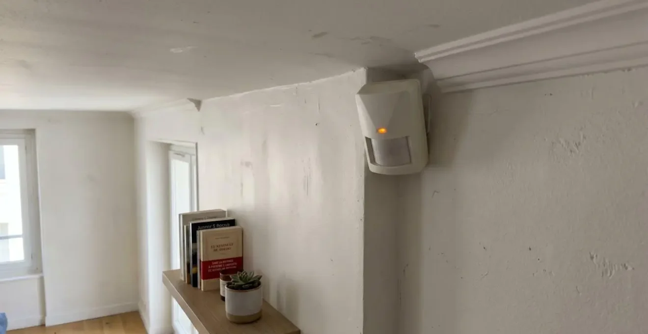 Détecteur de mouvement infrarouge blanc installé dans l'angle supérieur d'une pièce résidentielle avec voyant LED discret